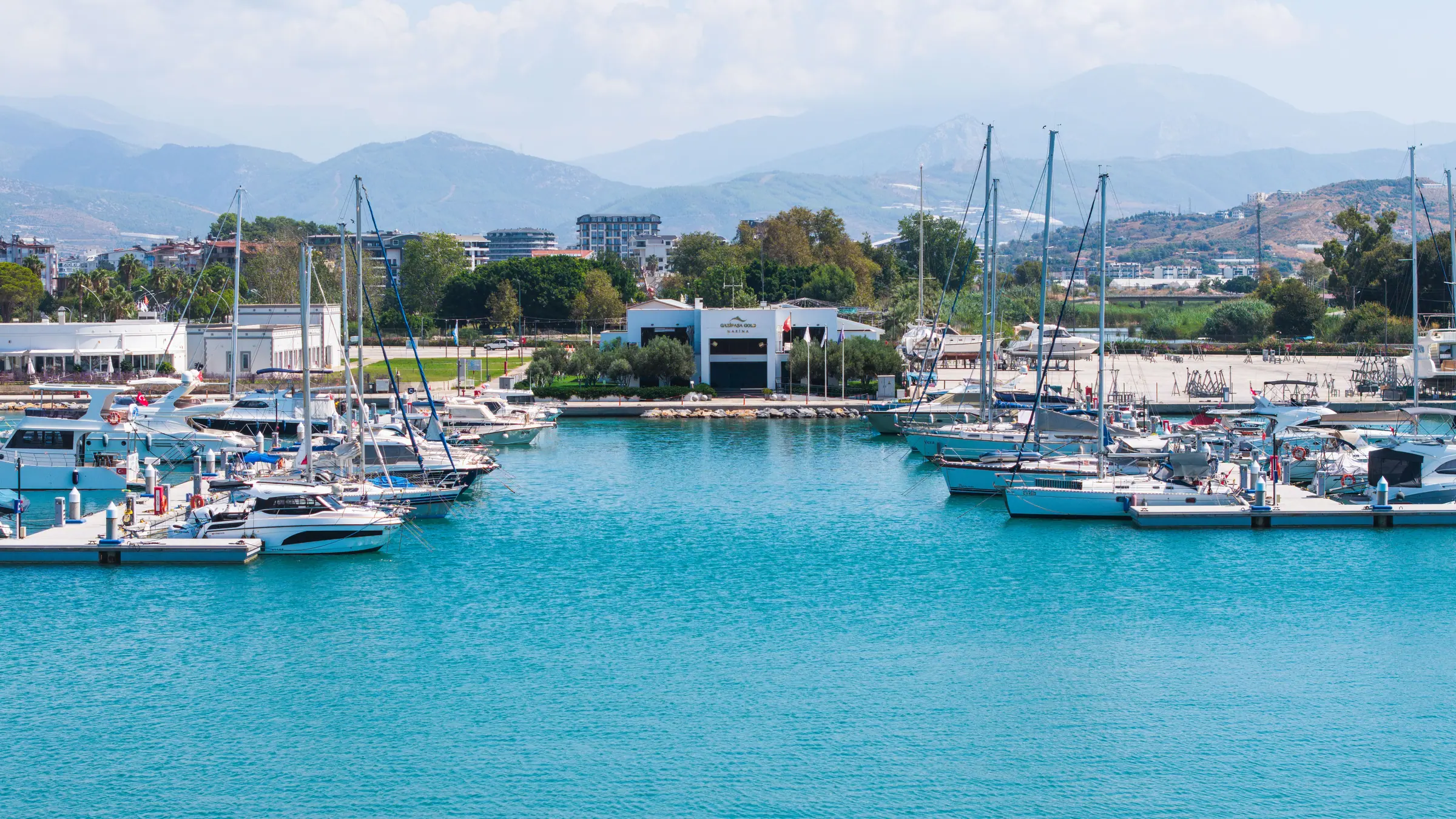 Gazipaşa Gold Marina iskelelerine bağlı yatlar ve arkada marina binası, Toros Dağları